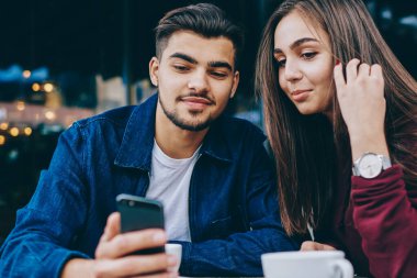 Genç hale ve kadın hipsters iyi wifi bağlantısı ile akıllı telefon video izlerken kafede birlikte kahve molası harcama, adam boş zamanlarında kız arkadaşı için cep telefonları için modern bir uygulama gösteren