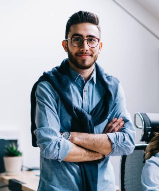 Pozitif başarılı adam uzman yarım uzunlukta portre ofis iç çapraz kolları ile ayakta iken kamera bakarken meslektaşları arka plan, iş ve meslek konuşurken