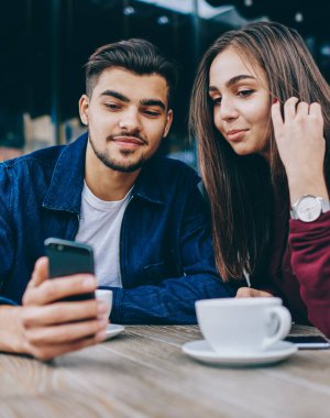 Genç hale ve kadın hipsters iyi wifi bağlantısı ile akıllı telefon video izlerken kafede birlikte kahve molası harcama, adam boş zamanlarında kız arkadaşı için cep telefonları için modern bir uygulama gösteren