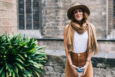 Şık şapkası ve atkısı olan oldukça modern bir kadın. Ortaçağ tuğla binasında yürüyor, camları rendeliyor ve heyecan verici şehir turunda kahve içiyor.