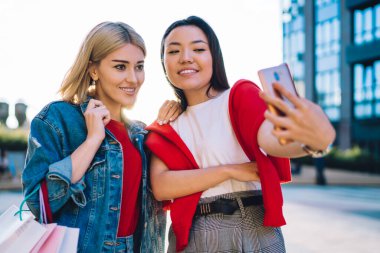Mutlu genç ve çeşitli çekici kız arkadaşlar günlük kıyafetlerle cep telefonundan selfie çekiyorlar. Şehir sokaklarında birlikte alışveriş yaptıktan sonra.