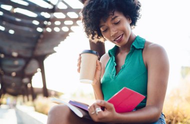 Edebiyat hobisi için eğlenen ve doğa ortamında boş zamanlarında en sevdiği romantik kitabı okuyan pozitif siyah kız öğrenci.