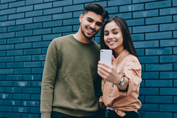 Cheerful couple in love dressed in casual posing for selfie on smartphone camera standing together,young smiling teen hipster girl and guy using modern mobile phone application making common picture