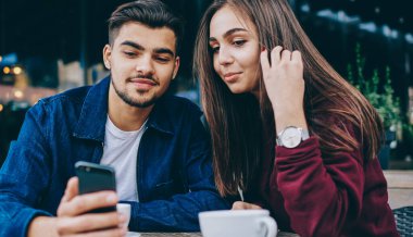 Genç hale ve kadın hipsters iyi wifi bağlantısı ile akıllı telefon video izlerken kafede birlikte kahve molası harcama, adam boş zamanlarında kız arkadaşı için cep telefonları için modern bir uygulama gösteren