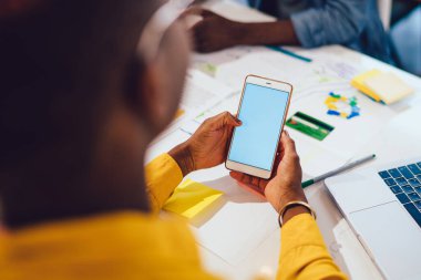 İş ortağıyla iş birliği yaparken dizüstü bilgisayarı ve cep telefonunu izleyen kimliği belirsiz siyahi bir çalışanın arka plan görüntüsü