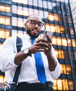 Resmi kıyafetler giymiş, gözlüklü Afrikalı Amerikalı girişimciler şehir merkezindeki caddede dikilip binalar ve akıllı telefonlara bakıyorlar.