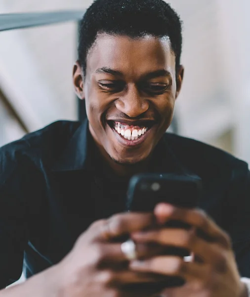 Cheerful excited black man reading positive news in social network using 4g connection on modern cellphone, happy dark skinned male watching funny comedy content via application on smartphone