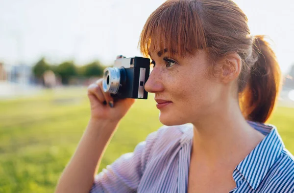 Çekici beyaz kadın, elinde eski tip metal kamerayla fotoğraf çekerken odak noktasını kontrol ediyor. Kızıl saçlı hippi kız fotoğrafçı güneşli bir günde fotoğraf çekerek boş vakitlerini harcıyor.