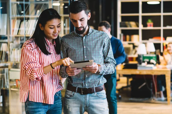 Zeki çoklu etnik kadın ve erkek, ahşap masalar ve öğrencilerle dolu geniş bir kütüphanede kağıt tablet çizmekten bahsediyorlar.