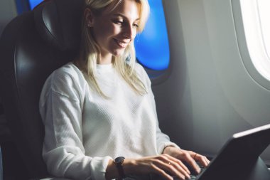Gülümseyen kadın uçak yolcusu klavye bilgisayarında, içinde kablosuz internet erişimi olan modern havayolu üzerinde uçarken. Serbest çalışan genç bir kadın gezgin.