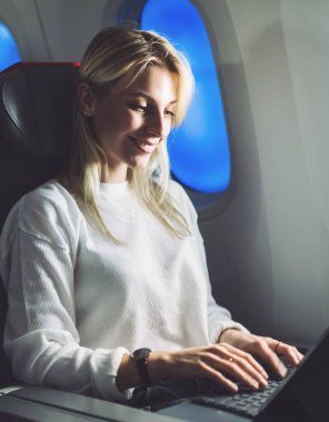Gülümseyen kadın uçak yolcusu klavye bilgisayarında, içinde kablosuz internet erişimi olan modern havayolu üzerinde uçarken. Serbest çalışan genç bir kadın gezgin.