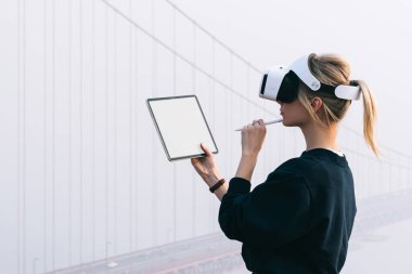 Sanal gerçeklik gözlüğü takıp kulaklıkla 3 boyutlu mühendislik inşaatı yapmayı planlayan düşünceli beyaz kadın modern dokunmatik rampada çalışıyor. Geliştirilmiş mimari ile VR yenilikçi yüksek teknoloji