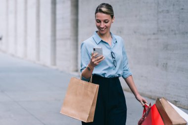 Neşeli kadın moda blogcusu, şehir merkezinde yürürken ve Kara Cuma satışları olan bir markayı ararken kendi web sitesindeki takipçilerin mesajlarını ve yorumlarını kontrol ediyor.