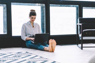 Düşünceli genç bir kadın modern dizüstü bilgisayarda çalışıyor şık bir dairede kablosuz internet bağlantısı kullanıyor. Konsantre olmuş hippi kız bilgi arıyor ve uygulama yüklüyor.