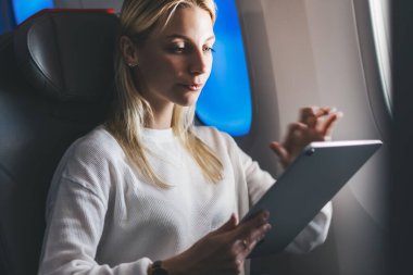 Sarı saçlı beyaz bir kadın, internet erişimini kullanarak büyük tablet bilgisayardan online alışveriş yapıyor. Dijital göçebe. Kablosuz uçuş sırasında kablosuz bağlantı kuran kadın turist.
