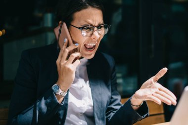 Resmi giyinmiş öfkeli bir kadın, içerik web sitesinde kendi şirketinin sorunları hakkında haberler okuyor ve uluslararası akıllı telefon konuşmaları sırasında çalışanlara bağırma ve yangın çağrısı yapıyor.