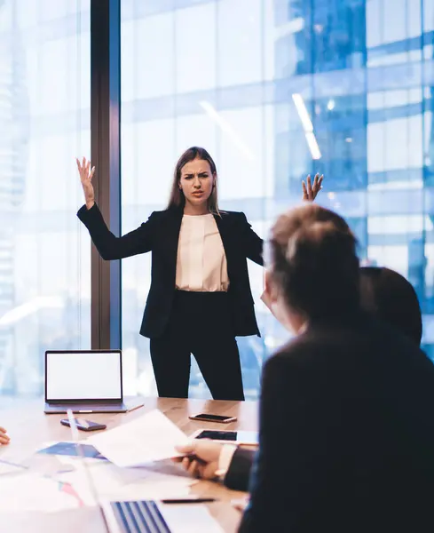 Confused female director complains to employees during meeting on office interior. Businesswoman carrying presentation with expressions while standing near table,group of business people brainstorming
