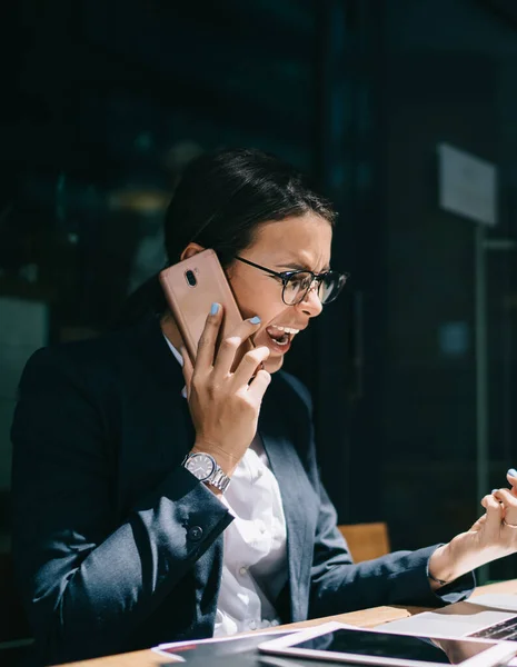 stock image Aggressive caucasian female director reading message with financial report and calling to manager for shouting using roaming internet connection on smartphone gadget and cafeteria wifi on laptop