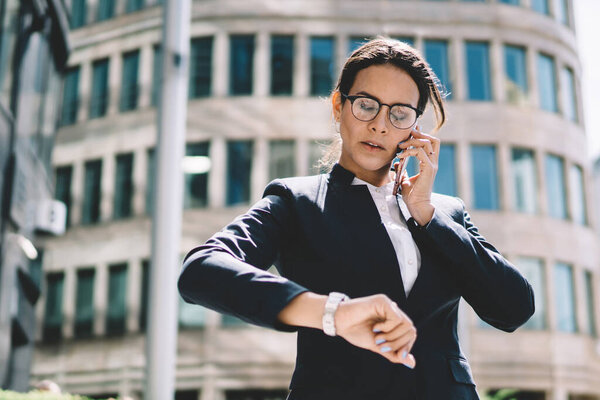 Attractive confident female boss calling to employee for clarify time of meeting in business district, serious woman dressed in formal suit making important internet