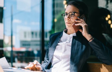 Beyaz kadın avukat resmi giysiler içinde müşteriyle yaptığı gezici sohbetler sırasında başını çevirimiçi iş için netbook 'la güneşli sokak kafeteryasında otururken başka tarafa bakıyor ve düşünüyor.