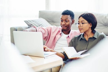 Pozitif Afro-Amerikan çifti laptopta alışveriş yapıyor ev içi internet sayfası, pozitif esmer tenli aile apartman dairesindeki netbook 'ta uygulamayı kullanarak video görüşmesi yapıyor.