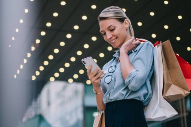 Elinde kese kağıtları olan şık bir kadın alışveriş merkezinin yakınında vakit geçirir ve akıllı telefon cihazından gelen mesajları okur. Cep telefonunda paket numarası olan mutlu hippi kız müşteri.