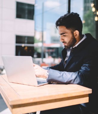 Konsantre olmuş Türk erkek ekonomist çalışma alanında modern dizüstü bilgisayarla mali rapor üzerinde çalışıyor ve veri bilgileri üzerinde kafa yoruyor, resmi giysi planlama stratejisinde ciddi bir bankacı