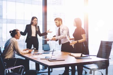 Bir grup erkek ve kadın işçi, gökdelen ofisinin iç kısımlarında büyük pencereli beyin fırtınası sırasında sorunları çözüyorlar.