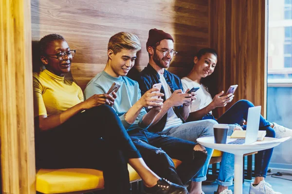 Addicted young people from social networks chatting online with followers on modern smartphones ignoring live communication during friendly meeting in modern coworking space