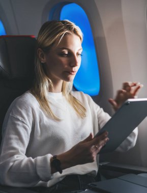 Sarı saçlı beyaz bir kadın, internet erişimini kullanarak büyük tablet bilgisayardan online alışveriş yapıyor. Dijital göçebe. Kablosuz uçuş sırasında kablosuz bağlantı kuran kadın turist.