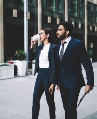 İş ortakları ile görüşmek üzere modern şehir sokaklarında yürüyen başarılı tüccarlar, iş arkadaşlarıyla iş yerinde dolaşırken zarif bir kadın kafein içeceği içiyor.