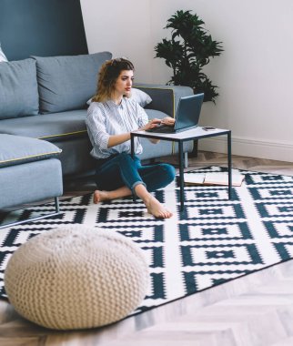 Modern apartmanda dizüstü bilgisayarda uzaktan çalışan düşünceli genç bir kadın. Kablosuz ev interneti kullanarak bilgisayar ödevi için konsantre hipster kız klavye metni.