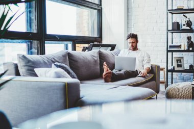 Milenyum adamı, dizüstü bilgisayarla kanepeye uzanmış sosyal ağlardan gelen takipçilerle mesajlaşmak için zaman harcıyor. Genç erkek uzaktan kumandalı işçi, Netbook 'ta yeni uygulamalar için bilgi arıyor.