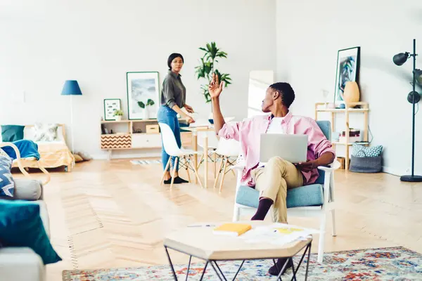 stock image Dark skinned hipster guy working at home at laptop computer raise hand for asking wife favor or help , young african american marriage spending free time at modern designed living room interior