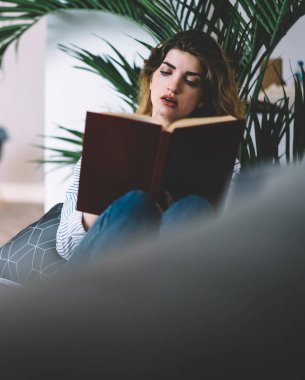 Modern apartman dairesinde ilginç ders kitapları okuyan konsantre genç bir kadın. Düşünceli hippi kız kendi evinde kanepede uzanmış kitaptan bilgi öğreniyor.