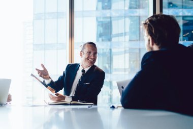 Şirket meslektaşları ofis içinde toplantı masasında oturup gülümseyen erkek yöneticilerle fikir alışverişinde bulunuyorlar. Yaratıcı stratejileri ve beyin fırtınalarını paylaşan bir grup işçi