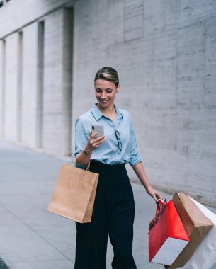 Neşeli kadın moda blogcusu, şehir merkezinde yürürken ve Kara Cuma satışları olan bir markayı ararken kendi web sitesindeki takipçilerin mesajlarını ve yorumlarını kontrol ediyor.