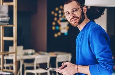 Gözlüklü, genç ve başarılı bir adam taşınabilir bilgisayar kullanarak yayını düşünmekten alıkoyuyor. Dijital cihaz tutan erkek hipster ve birlikte çalışma ofisindeki bilgileri taramak için kablosuz internet kullanıyor.