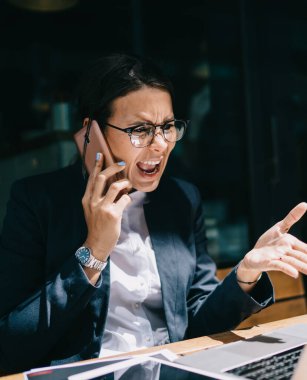 Resmi giyinmiş öfkeli bir kadın, içerik web sitesinde kendi şirketinin sorunları hakkında haberler okuyor ve uluslararası akıllı telefon konuşmaları sırasında çalışanlara bağırma ve yangın çağrısı yapıyor.