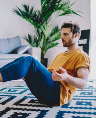 Genç adam evde sağlıklı yaşam tarzını ve spor vücut şeklini destekleyen yoga egzersizleri yapıyor. Kaliteli iç dekorasyonla birlikte. Hippi adam sabah antrenmanı sırasında düz alanda meditasyon yapıyor.