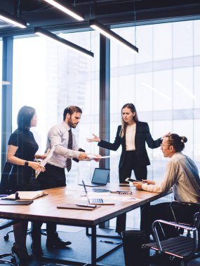 Bir grup erkek ve kadın işçi, gökdelen ofisinin iç kısımlarında büyük pencereli beyin fırtınası sırasında sorunları çözüyorlar.