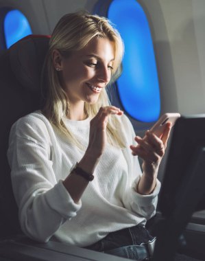 Kablosuz ağ erişimiyle rahat uçuşun tadını çıkarırken cep telefonundan mesaj atan beyaz kadın yolcu. Genç turist kadın internet bağlantısı olan havayolu şirketini seçti
