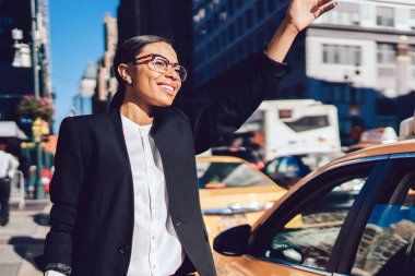 Neşeli, başarılı bir kadın, iş ortaklarıyla iş görüşmesine gittiği için taksiyi selamlıyor. Mutlu, gülümseyen bir kadın, modern finans bölgesinde taksi çağırıyor.