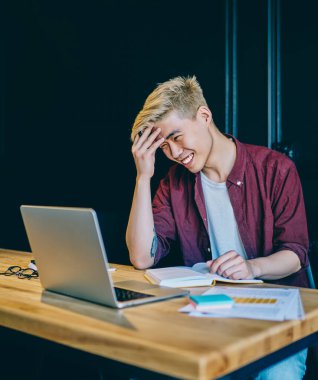 Modern uzayda dizüstü bilgisayarla Webinar 'ı izlerken gülen Çinli olumlu hippi, sosyal ağdan komik haberler okuyan neşeli Asyalı genç adam.