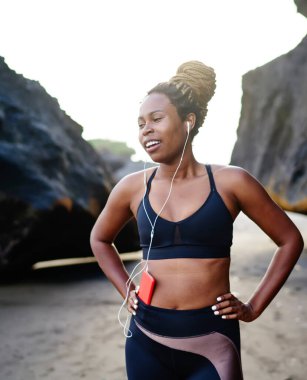 Mutlu yorgun afro amerikan kadın koşucu aynı anda koşu ve duygu keyfi mola yapma, genç siyah sportif kadın rock yakın sabah egzersiz sırasında kulaklık la müzik çalma listesi dinleme