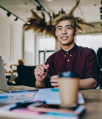 Neşeli gülümseyen Asyalı hippi öğrenci bayan meslektaşıyla aynı masada oturuyor ve içeride işbirliği yaptığı için kendini iyi hissediyor, başarılı arkadaşlar birlikte çalışma alanında bilgisayar kullanarak öğreniyor.