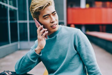 Sıradan giyinmiş yakışıklı Çinli hippi, akıllı telefon cihazıyla arıyor şehir ortamında oturuyor ve başka tarafa bakıyor. Japon genç blog yazarı modern cep telefonuyla konuşuyor.