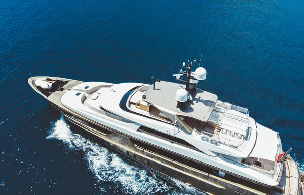 Aerial view of luxury yacht goes to open sea with beautiful blue colour of water. Wealth recreation lifestyle. Birds eye view of expensive floating ship traveling by Europe in summer
