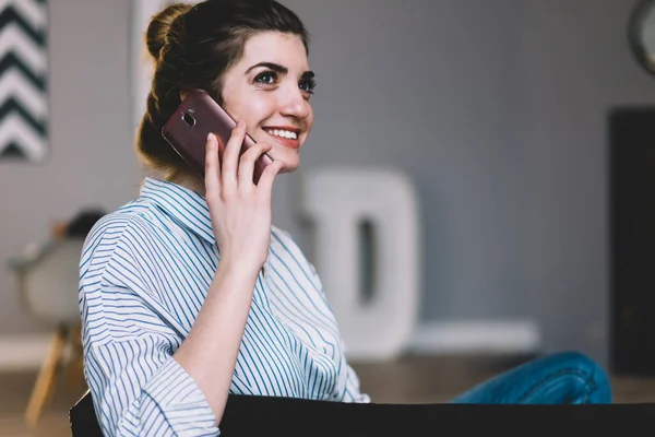 Stock image Cheerful young woman laughing while calling on smartphone device and discussing news with friend during conversation.Positive cute hipster girl communicating on mobile phone relaxing at home