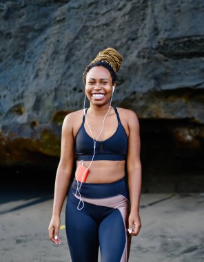 Kulaklıklı müzik uygulamasından ses şarkıları dinlerken kameraya gülümseyen mutlu afro amerikalı genç kadının portresi, spor eşofman giymiş neşeli koyu tenli koşucu heyecanlı